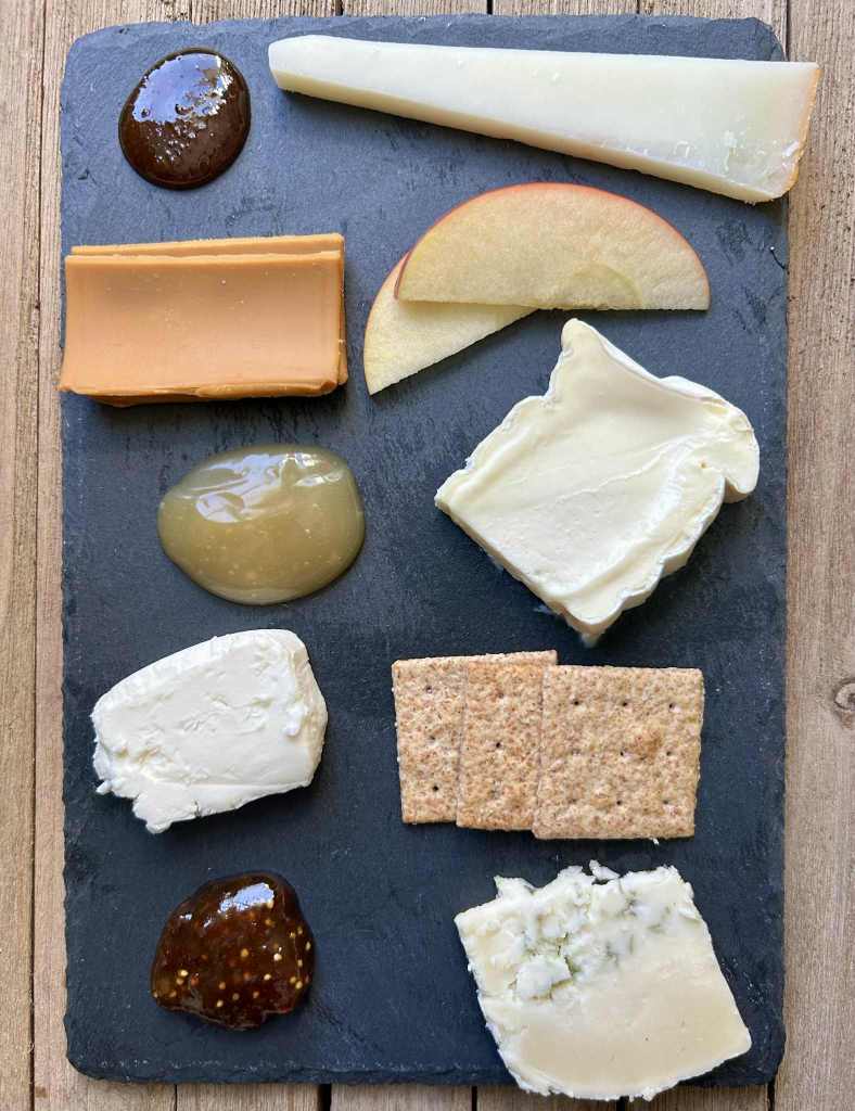 a slate plate of various cheeses and accompaniments