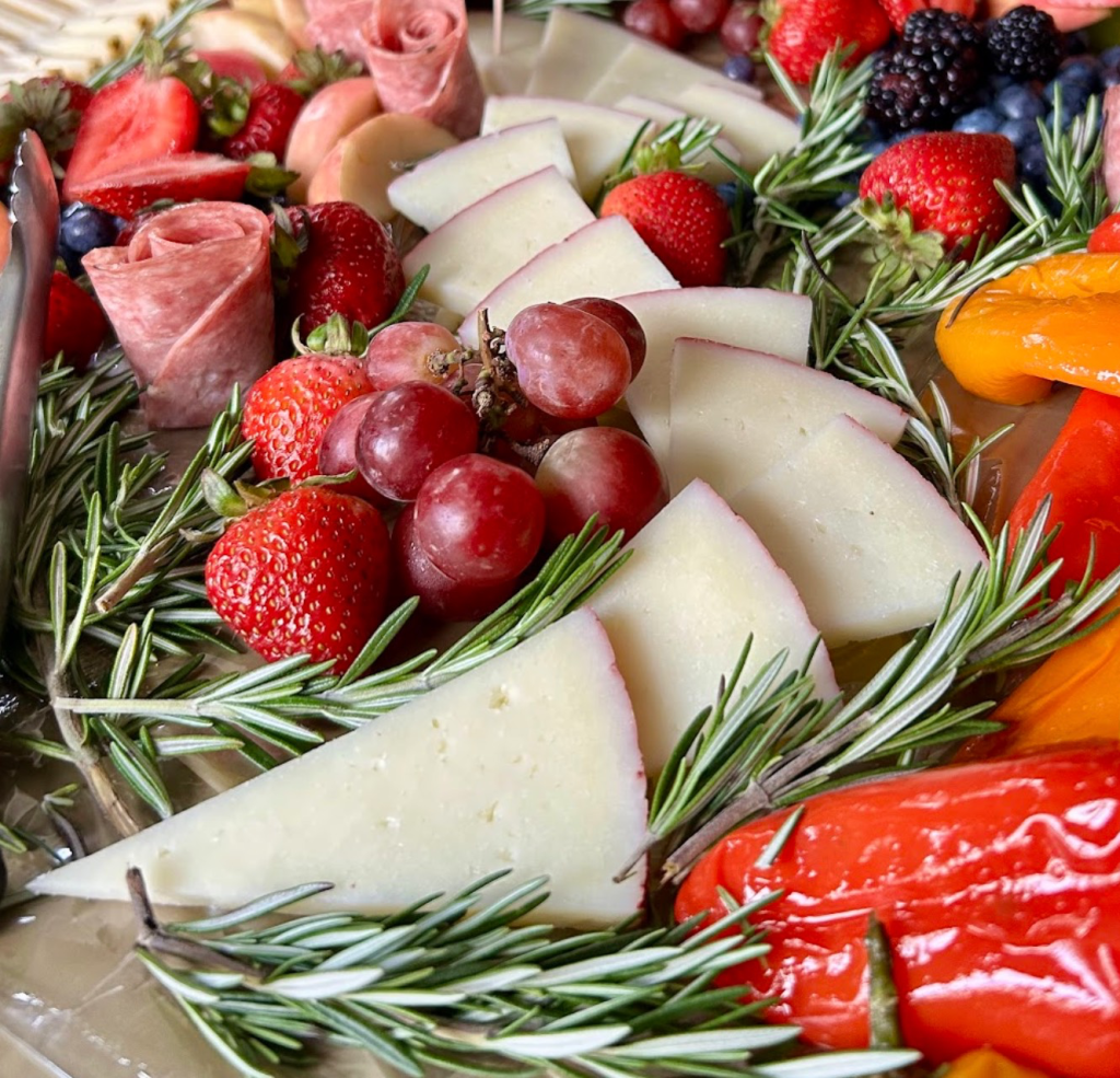 an antipasti platter with cheese, roasted peppers, fruit, and salami